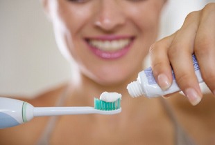 woman putting toothpaste onto an electric toothbrush