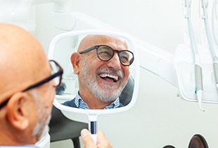 A senior man admiring his treated smile with a hand mirror 