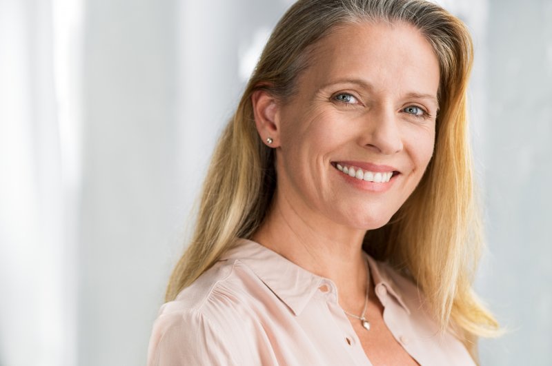 an older woman wearing a pale pink blouse and smiling after receiving dental care with a soft tissue laser