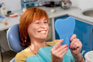 Woman smiling into mirror with her new dentures