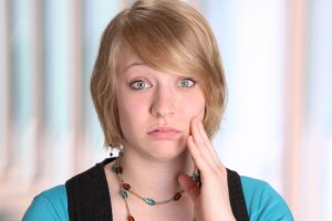 young woman with jaw pain holding her face