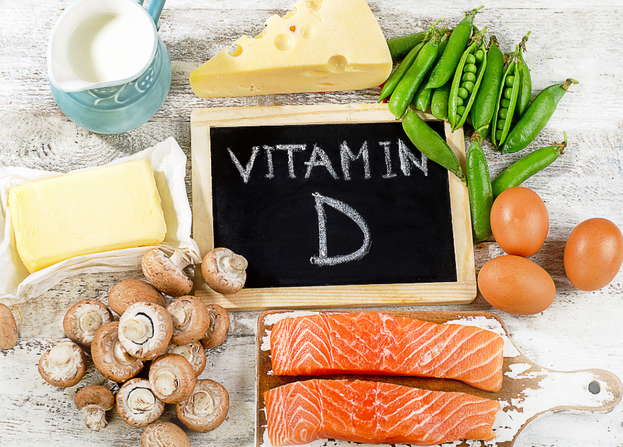 A small blackboard with "Vitamin D" written on it, surrounded by whole foods like cheese, eggs, green beans, butter, mushrooms...